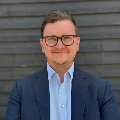 James Randall, Pre-Sales Engineer at Airwave Europe, wearing glasses and a navy blazer, standing in front of a dark wooden wall.